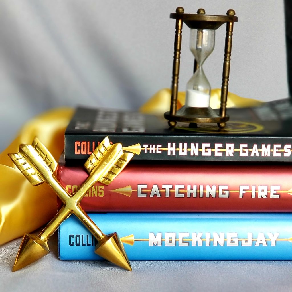 Stack of all three The Hunger Games young adult trilogy books with a small hourglass sitting on top of the stack