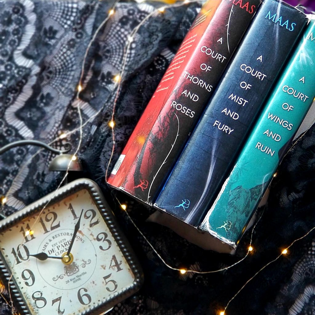 Looking down on all three books in the A Court of Thorns and Roses trilogy with a clock and small fairy lights